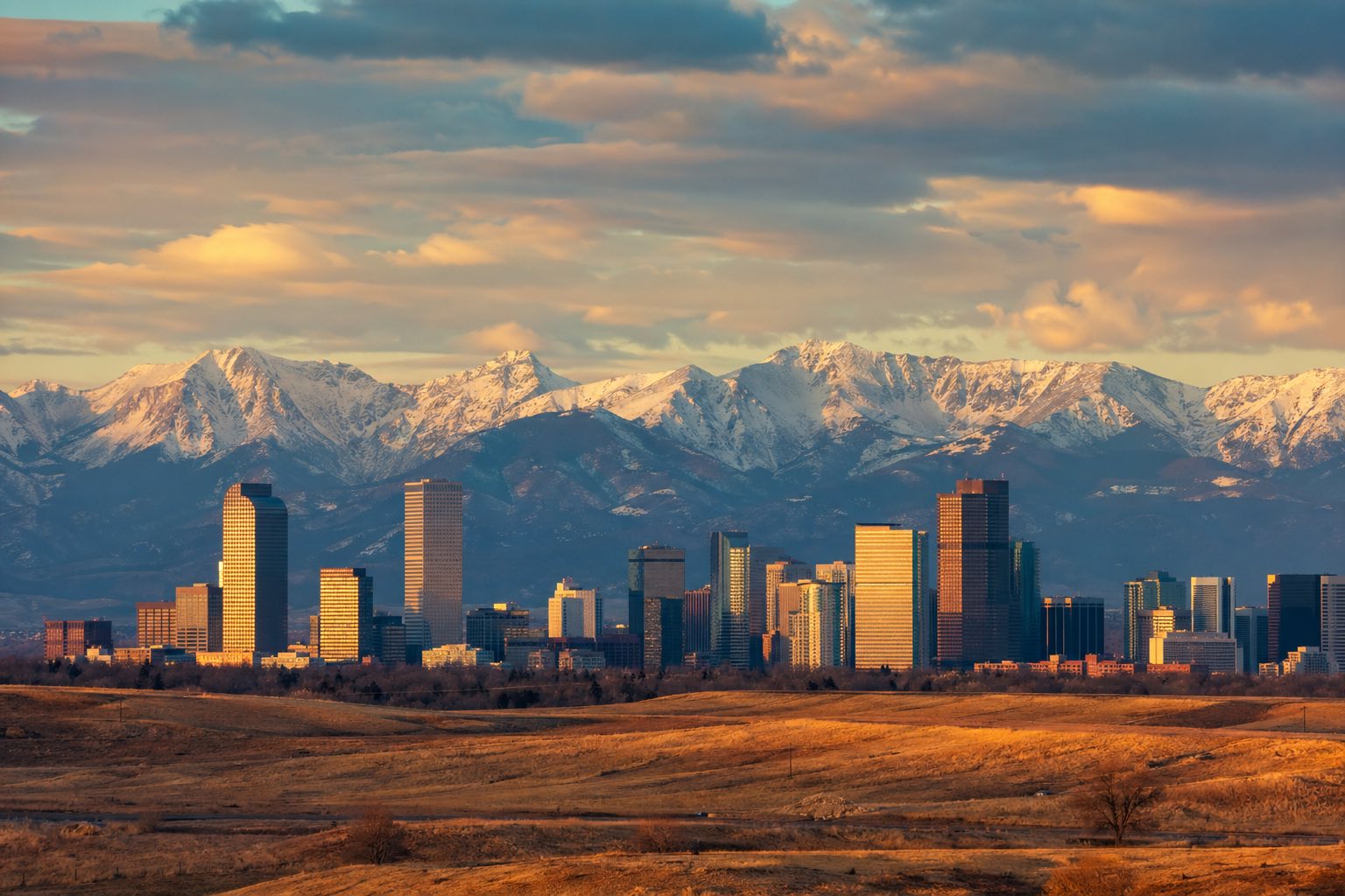 Modern photograph of the Denver skyline with the Rocky Mountains backdrop at golden hour representing Nation Movers' Colorado service area